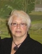 A woman with white hair and glasses is wearing black.